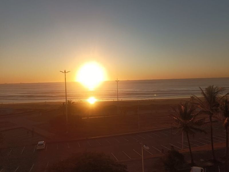 A scenic elevated view of the ocean coastline at sunset, showcasing the horizon and surrounding coastal landscape.