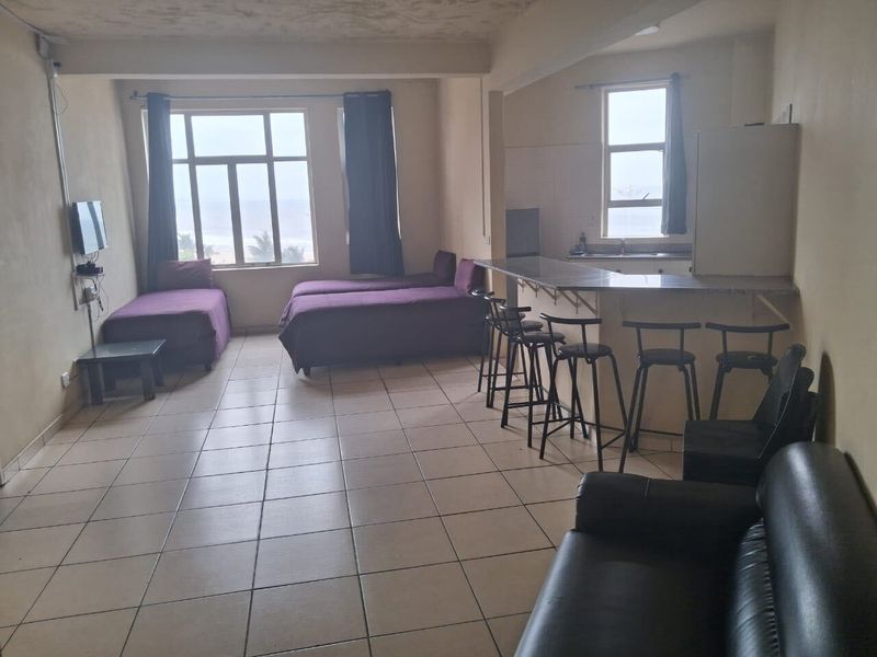 Open-plan living area featuring tiled flooring, a breakfast bar with kitchen sink, and large windows with ocean views.
