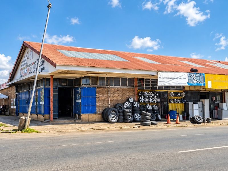 Commercial street-front property featuring a brick facade, corrugated metal roof, and security-gated access points, situated along a main road.