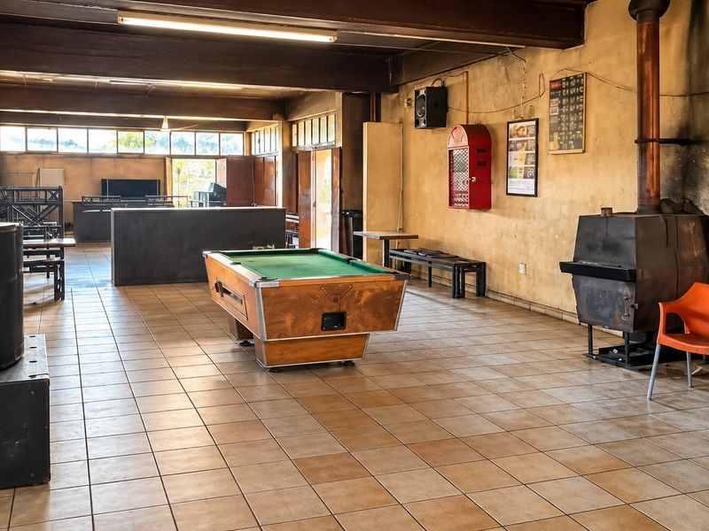Spacious open-plan commercial area featuring tiled flooring, exposed timber beams, and a built-in wood-burning fireplace, suitable for a bar or recreational venue.