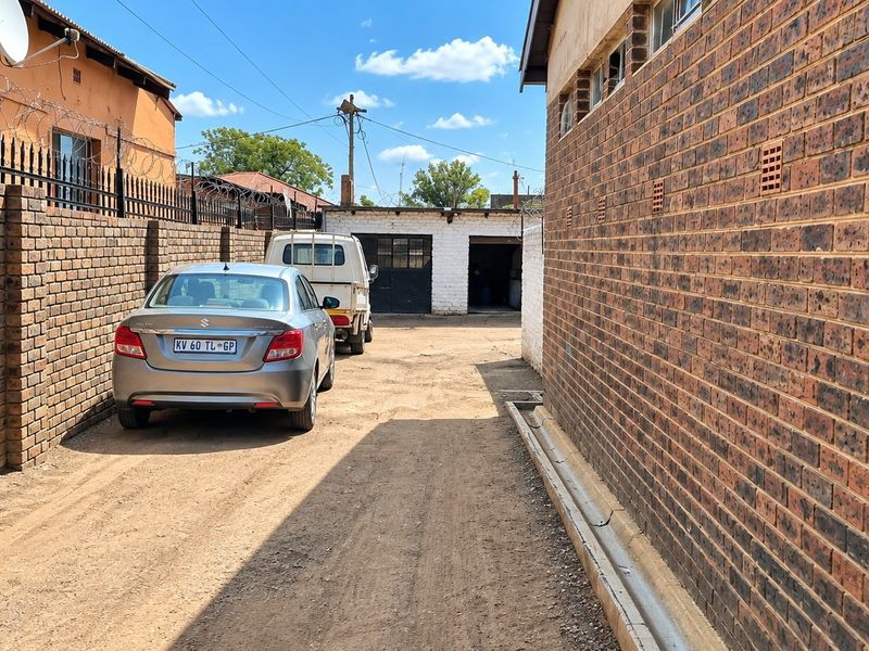 A rear exterior view showing a dirt driveway between two face brick boundary walls, leading towards a detached garage structure.