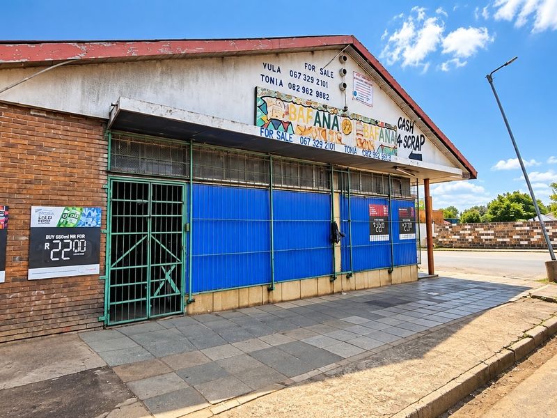 Front elevation of a commercial property featuring brick facade, metal security shutters, and a paved sidewalk area.