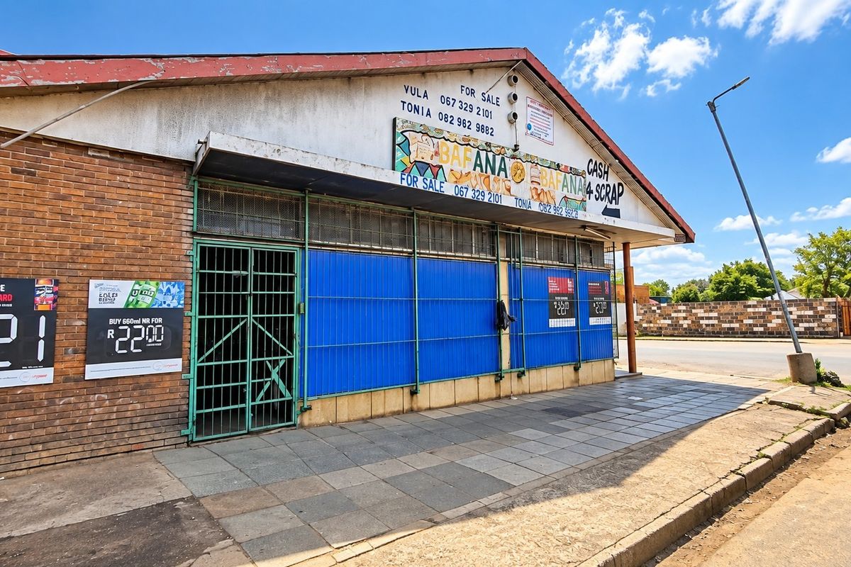 Front elevation of a commercial property featuring brick facade, metal security shutters, and a paved sidewalk area.