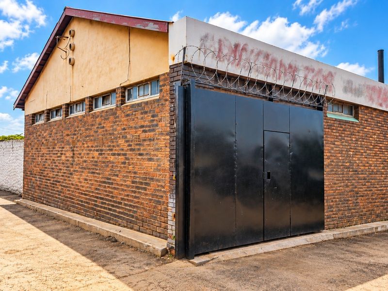 Rear exterior view of a commercial face brick building featuring a secure steel gate, razor wire fencing, and a concrete yard area.