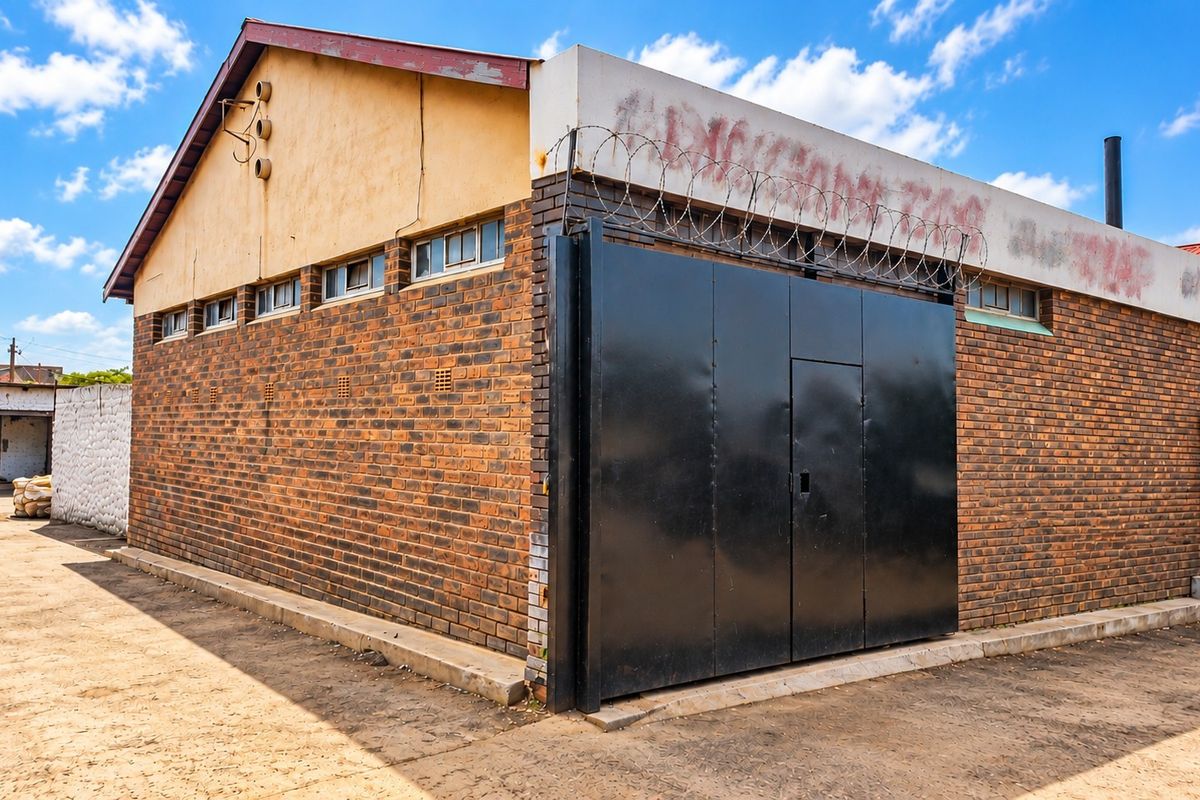 Rear exterior view of a commercial face brick building featuring a secure steel gate, razor wire fencing, and a concrete yard area.