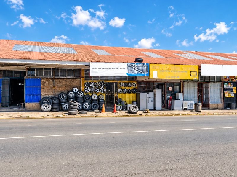 Commercial street-front property featuring a corrugated metal roof, brick facade, and multiple shopfront access points with security gates.