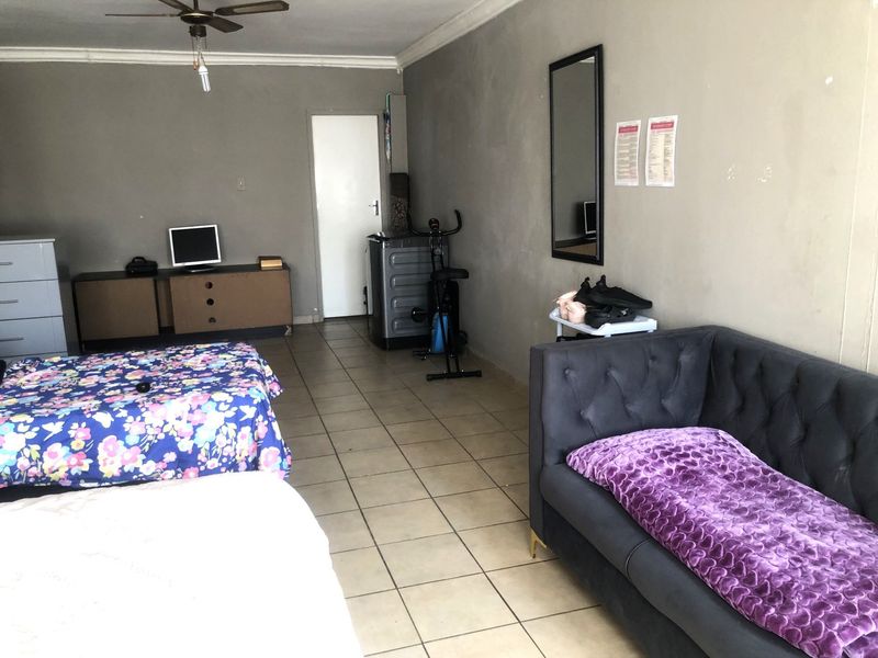 A spacious bedroom featuring tiled flooring, a ceiling fan, and neutral wall finishes, offering a versatile layout for various furniture arrangements.