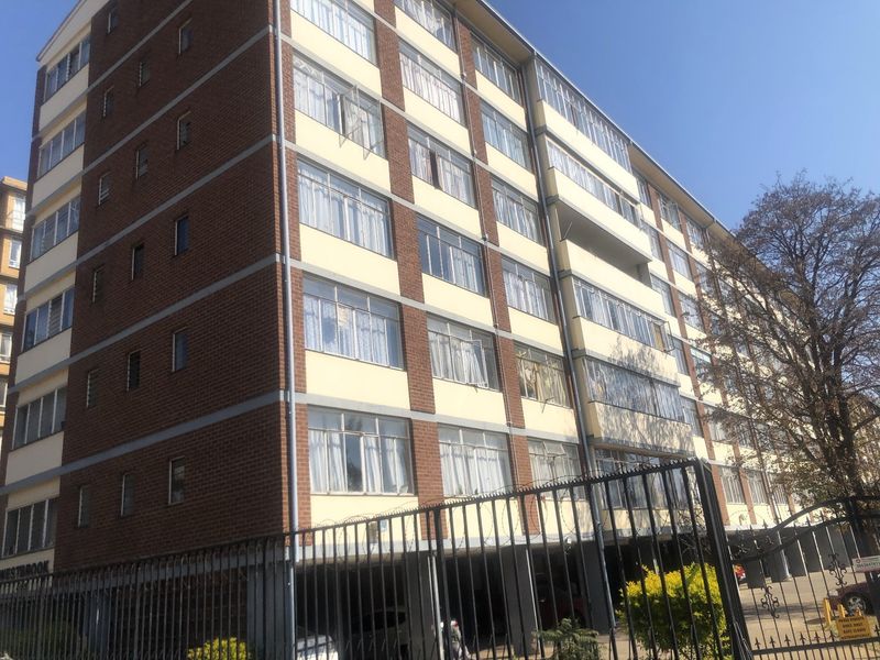 Exterior view of a multi-story apartment building featuring a brick and painted facade with secure perimeter fencing.
