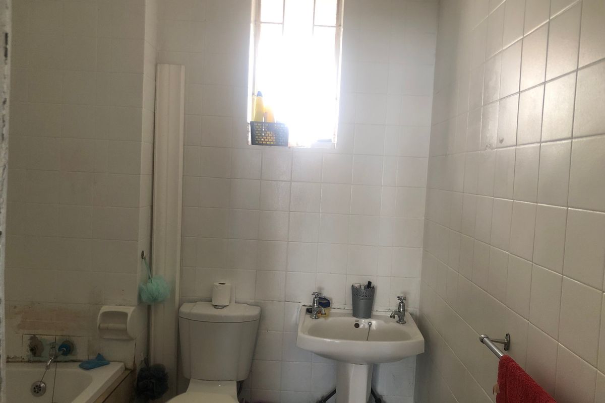 A functional bathroom featuring a pedestal basin, toilet, and bathtub with full-height wall tiling and a window for natural light.