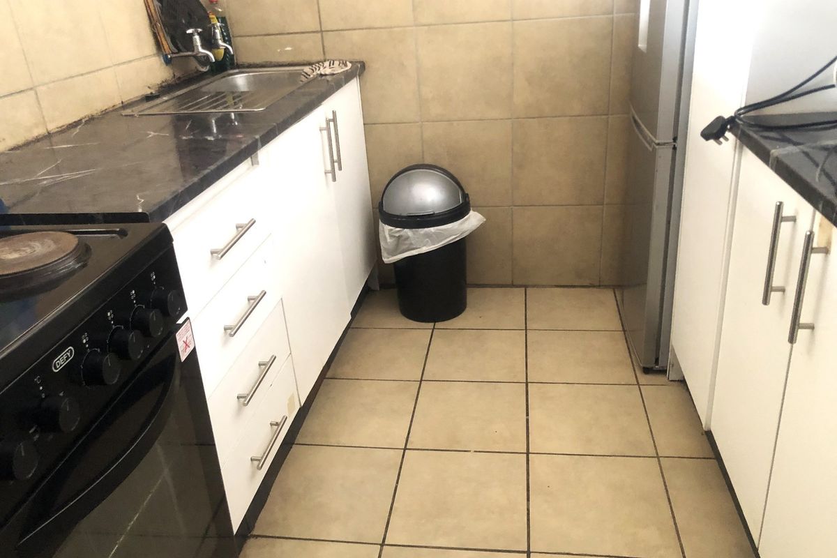 A functional kitchen featuring white cabinetry, dark laminate countertops, ceramic tiling, and a freestanding stove, offering a practical layout for daily meal preparation.