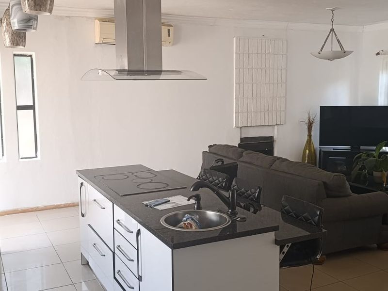Open-plan living area featuring a modern kitchen island with integrated hob and sink, tiled flooring, and split-system air conditioning.