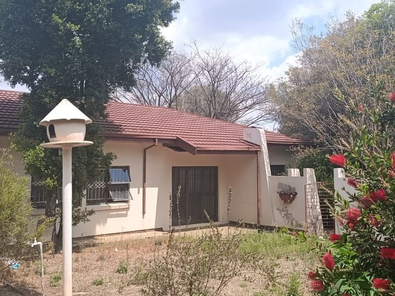 Rear view of the house featuring a tiled roof, security bars on windows, and a sliding door leading to an overgrown garden area.