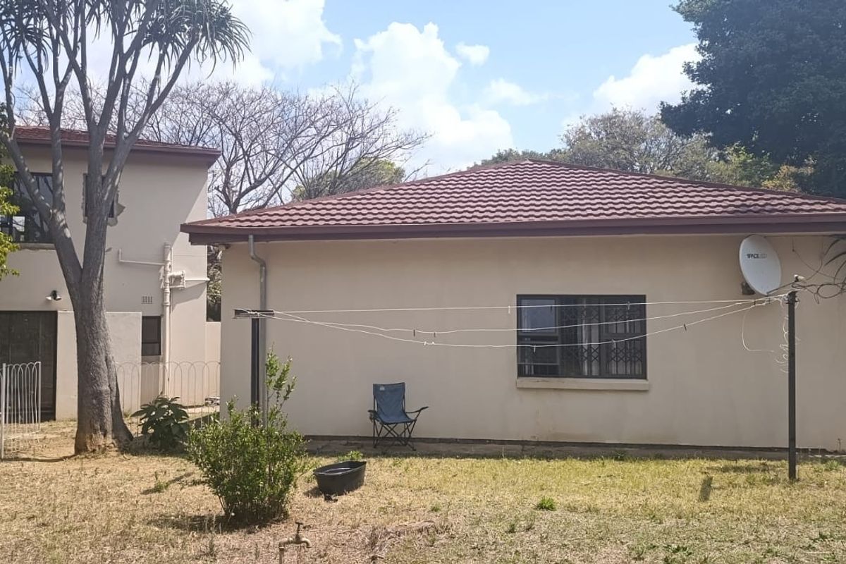 Rear view of the property showing the exterior wall, tiled roof, and garden area with security bars on the windows.