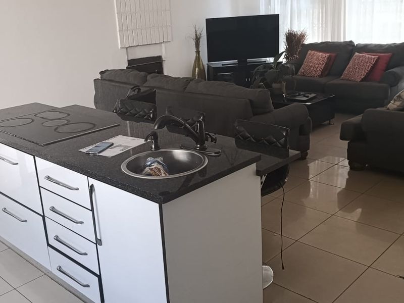Open plan living area featuring a modern kitchen island with granite countertops, integrated hob, and tiled flooring throughout the combined kitchen and lounge space.