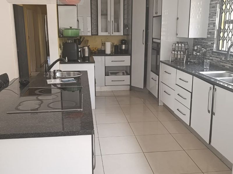 Modern kitchen featuring granite countertops, built-in oven, electric hob, double sink, and ample cabinetry with tiled flooring throughout.