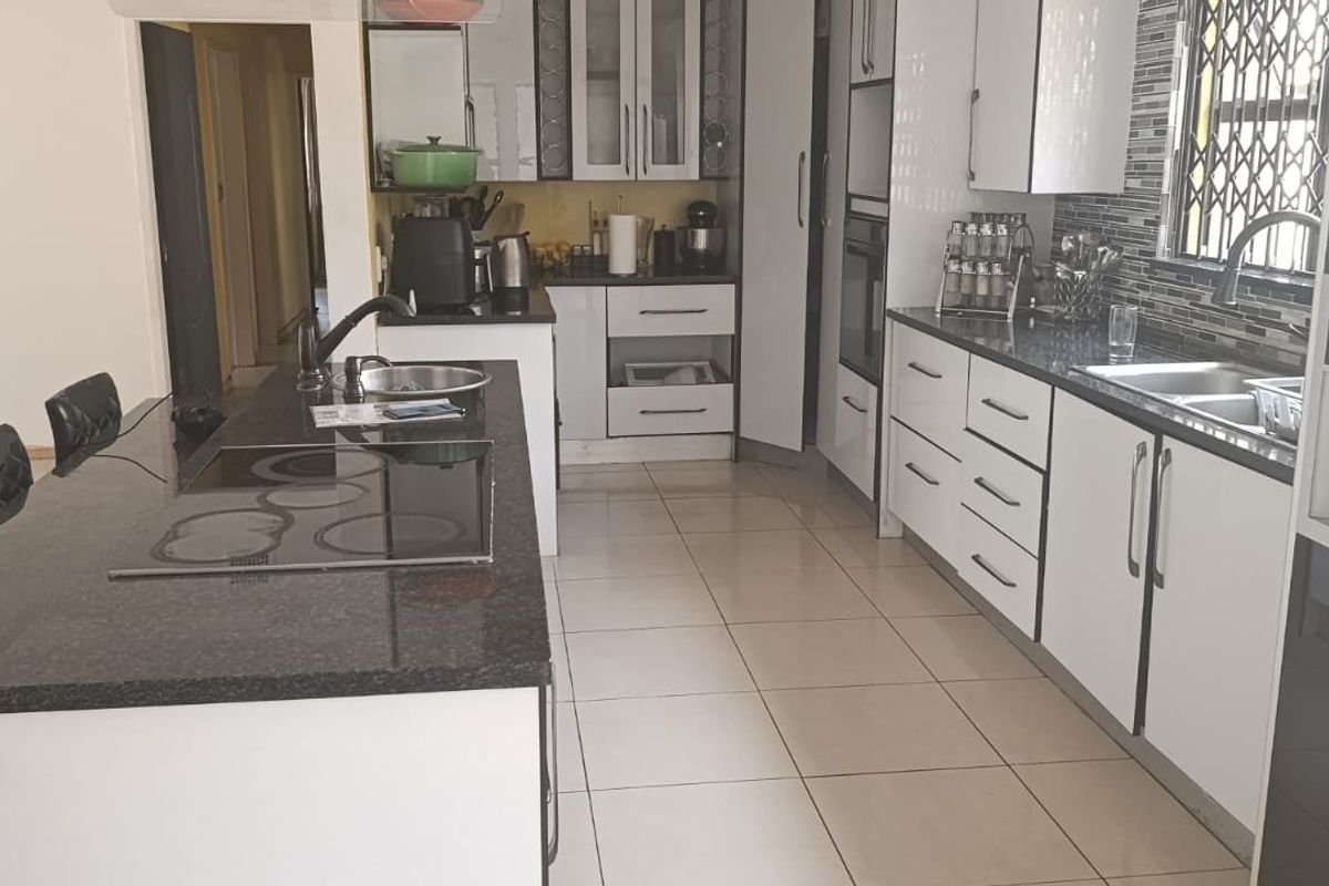 Modern kitchen featuring granite countertops, built-in oven, electric hob, double sink, and ample cabinetry with tiled flooring throughout.