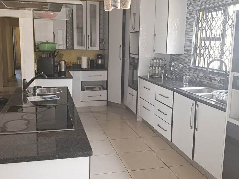 Modern kitchen featuring granite countertops, a central island with a built-in hob, ample cabinetry, and a double sink with tiled flooring.