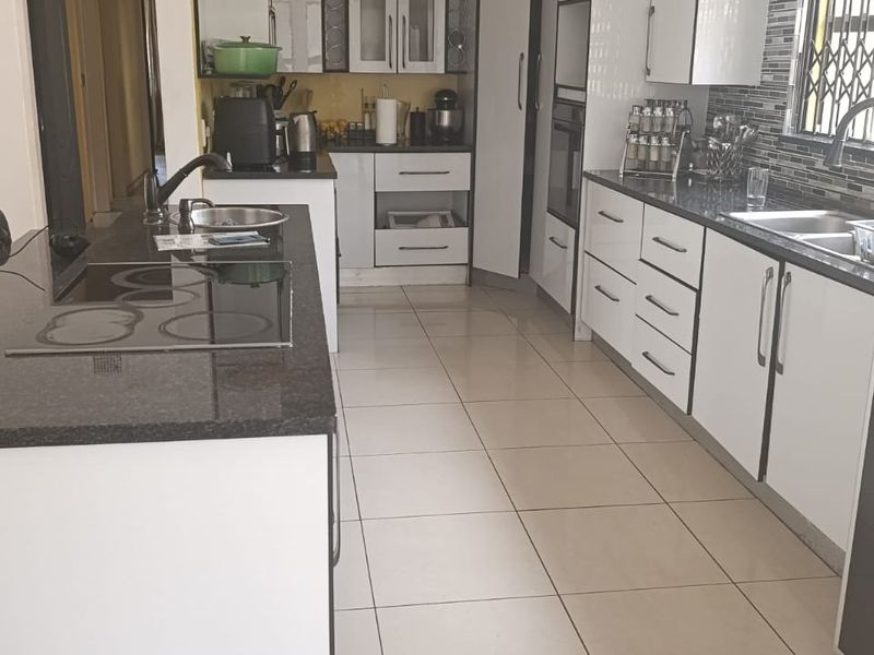 Modern kitchen featuring a central island with granite countertops, built-in oven, electric hob, double sink, and ample white cabinetry with tiled flooring.