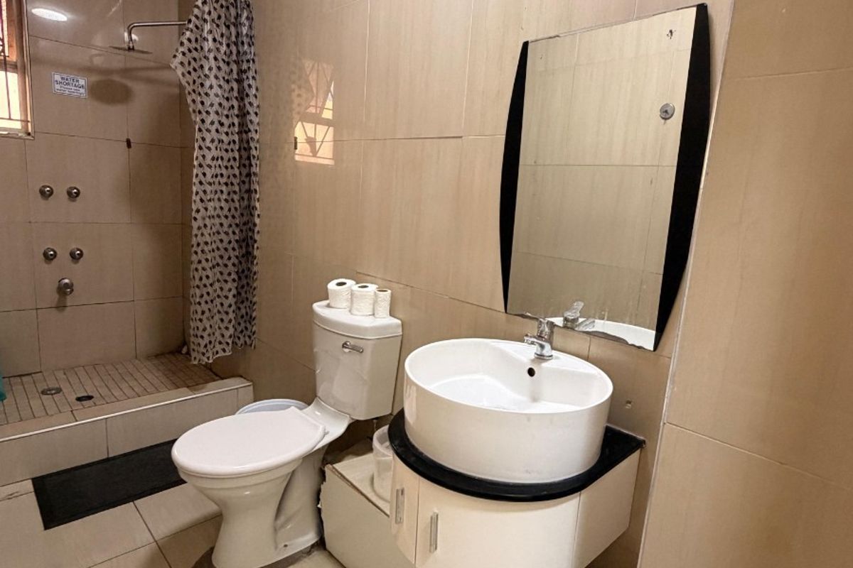 A functional bathroom featuring a wall-mounted vanity with a vessel sink, a toilet, and a tiled shower area.