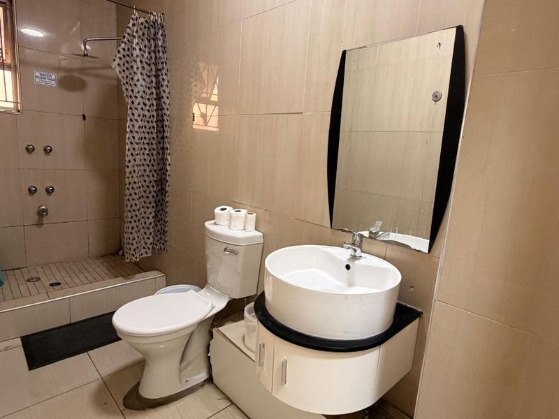 A functional bathroom featuring a wall-mounted vanity with a vessel sink, a toilet, and a tiled shower area.