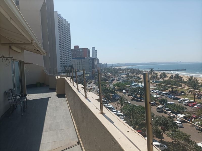 Spacious balcony featuring tiled flooring and a stainless steel balustrade, offering expansive views of the coastline and urban surroundings.