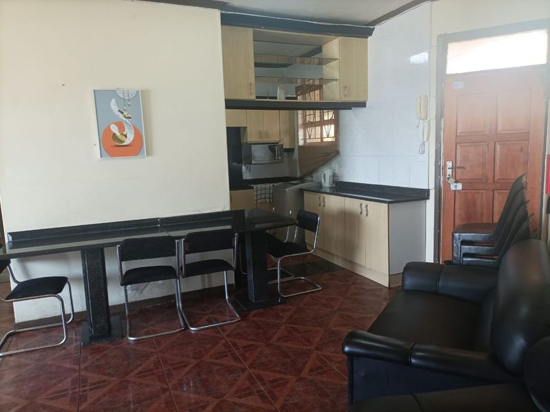 Open-plan living and kitchen area featuring built-in cabinetry, granite countertops, and tiled flooring, with direct access to the main entrance.