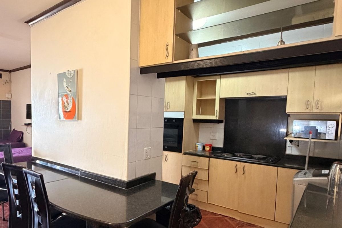 A functional kitchen featuring light wood cabinetry, dark granite countertops, a built-in oven, hob, and an integrated breakfast bar area.