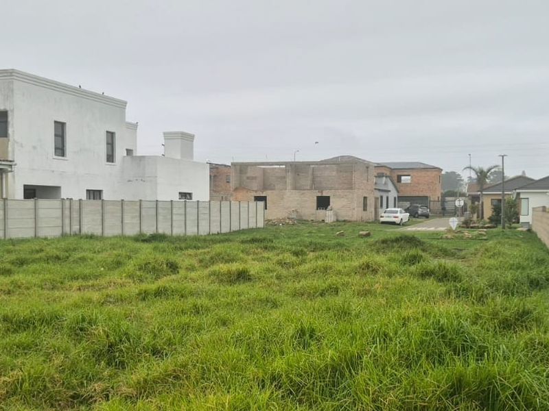 A vacant residential plot enclosed by precast concrete boundary walls, situated in a developed neighborhood with surrounding residential properties.