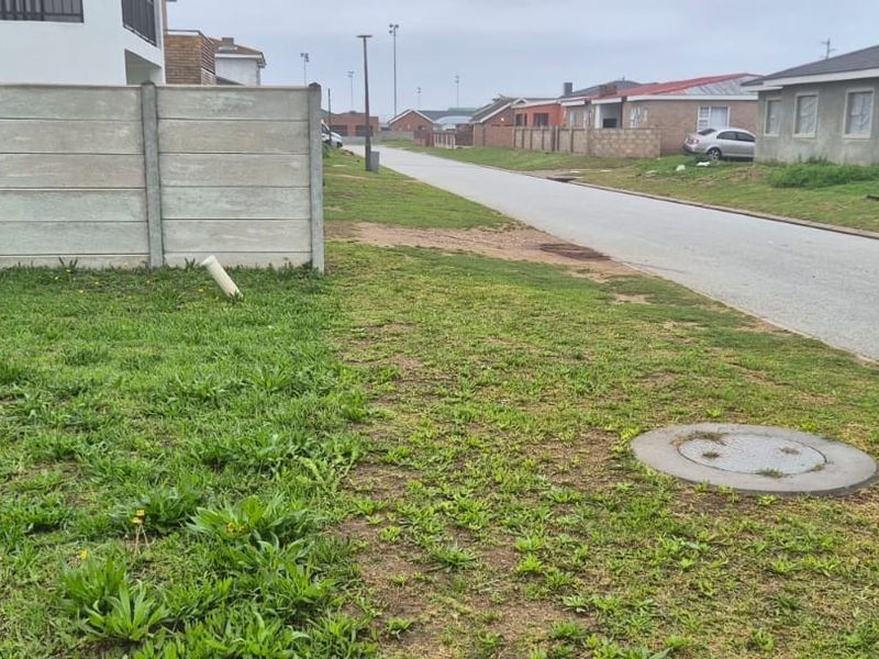 Street view of the vacant residential plot showing the boundary wall, access road, and surrounding neighborhood infrastructure.