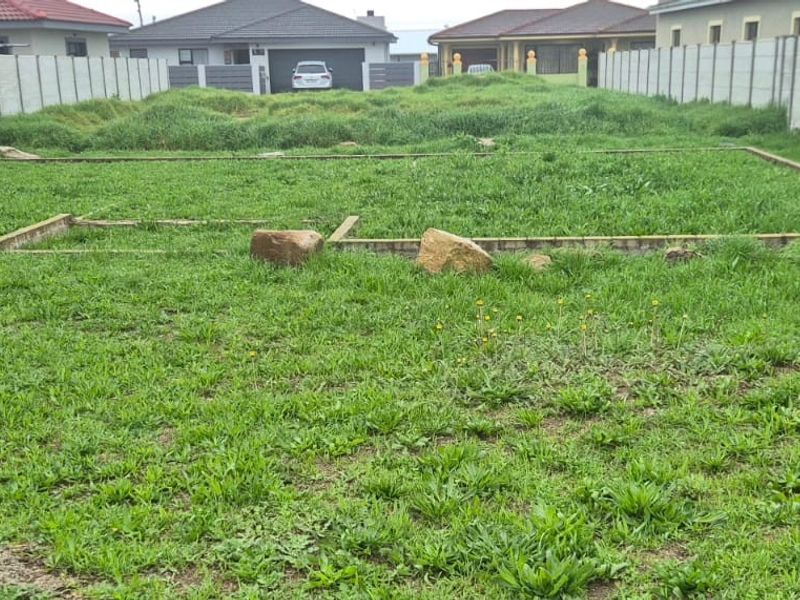 Vacant residential plot featuring a prepared foundation footing and enclosed by precast concrete boundary walls in a developed neighborhood.