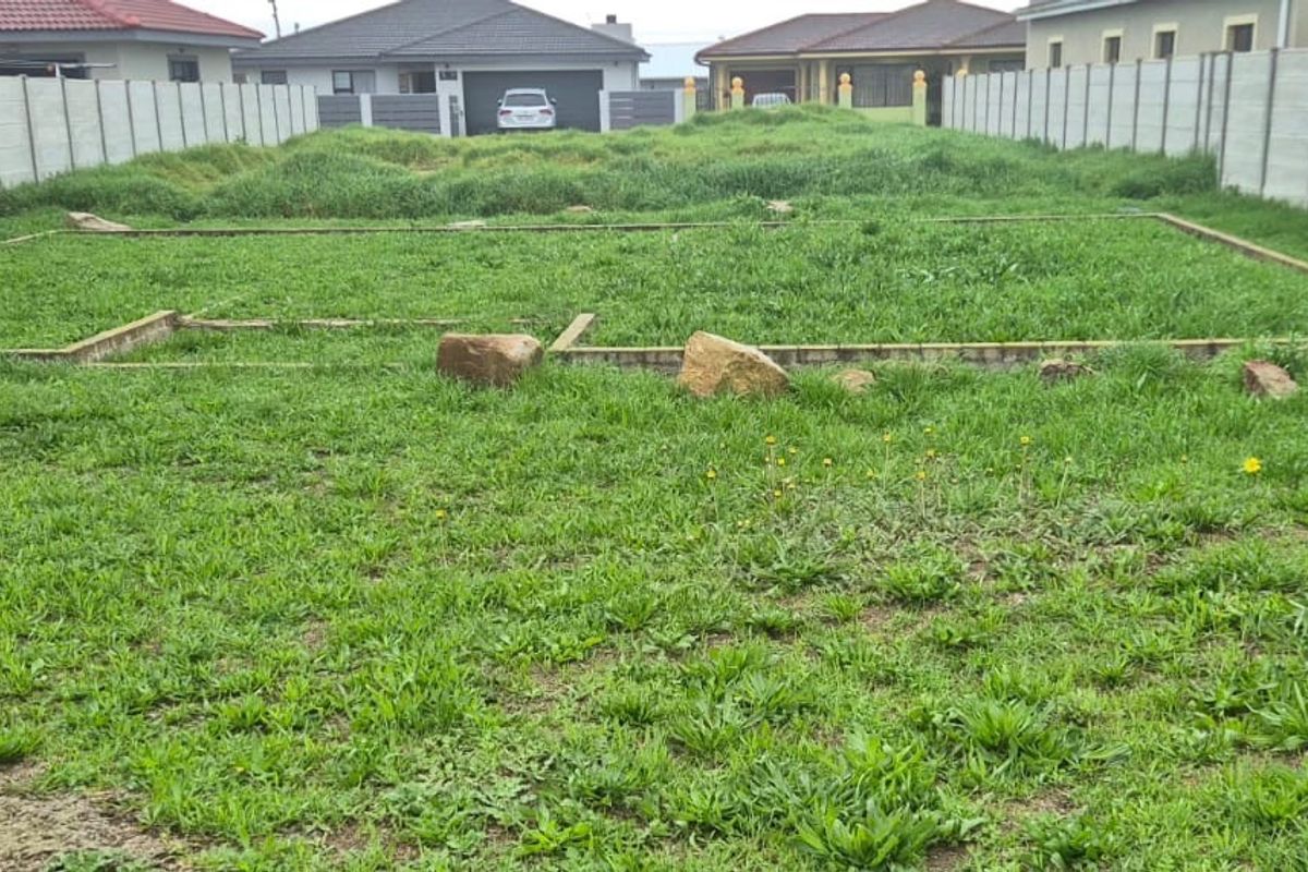 Vacant residential plot featuring a prepared foundation footing and enclosed by precast concrete boundary walls in a developed neighborhood.
