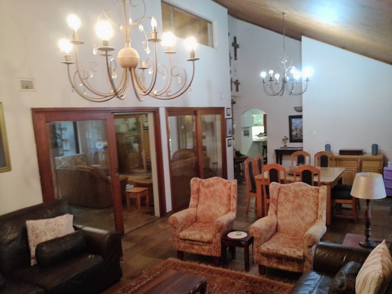 Spacious open-plan living and dining area featuring vaulted timber ceilings, large sliding glass doors, and classic wrought iron chandeliers.