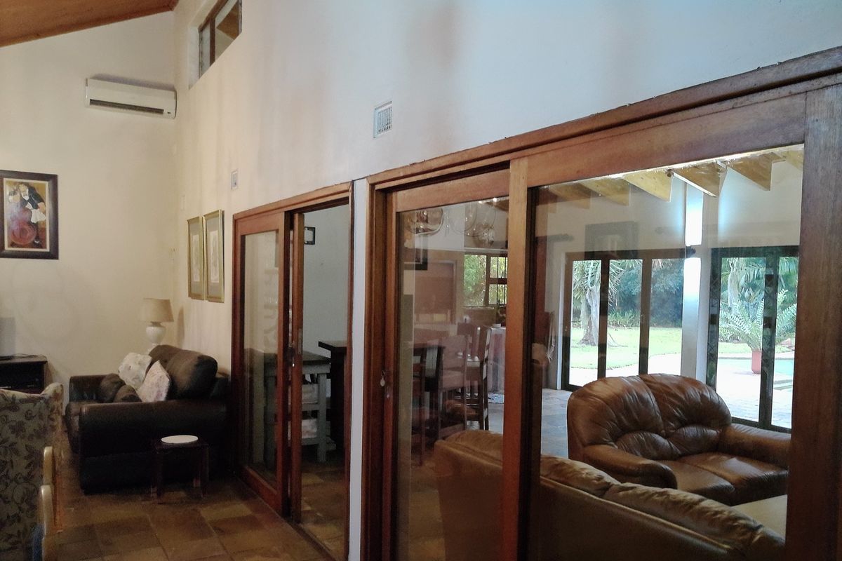 Spacious living area featuring vaulted timber ceilings, terracotta floor tiles, and large timber-framed sliding glass doors providing access to the outdoor patio area.