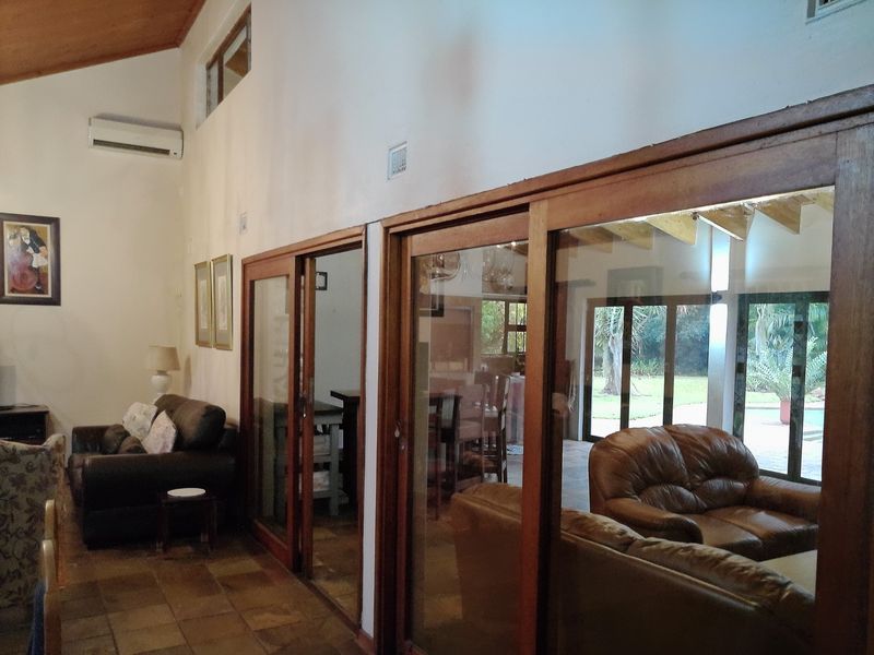 Spacious living area featuring vaulted timber ceilings, terracotta floor tiles, and large timber-framed sliding glass doors providing access to the outdoor patio area.