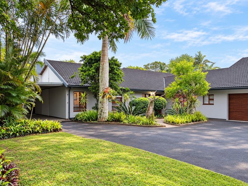 A well-maintained front exterior view of the house featuring a paved driveway, attached garage, carport, and established garden landscaping.