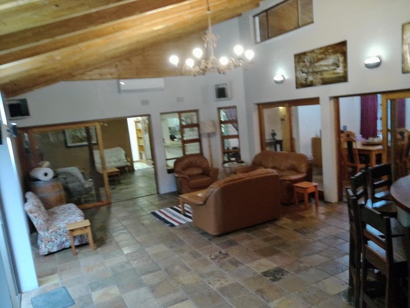 Spacious open-plan living area featuring vaulted ceilings with exposed timber beams, tiled flooring, and internal glass partitions connecting to adjacent rooms.
