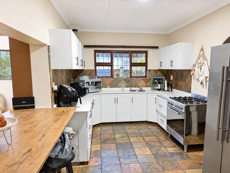A functional kitchen featuring white cabinetry, stone tile backsplash, slate flooring, and a stainless steel gas stove with an integrated breakfast bar.