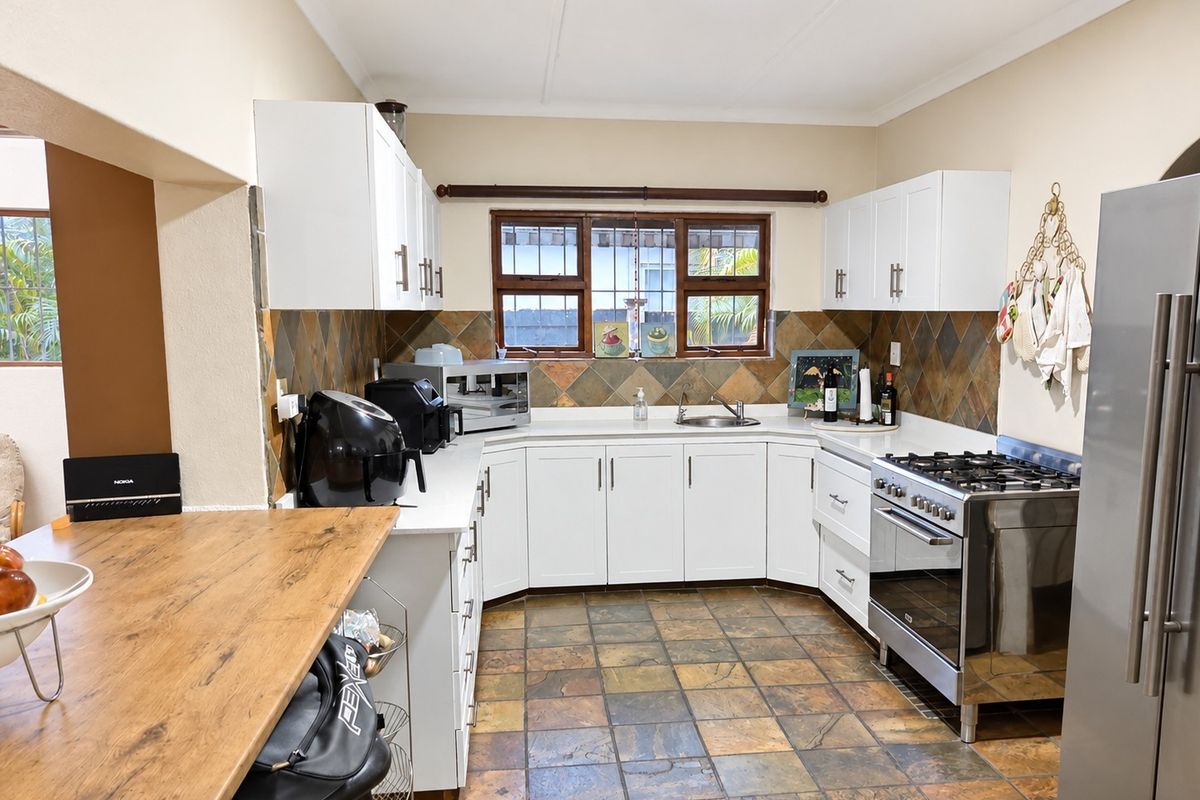 A functional kitchen featuring white cabinetry, stone tile backsplash, slate flooring, and a stainless steel gas stove with an integrated breakfast bar.