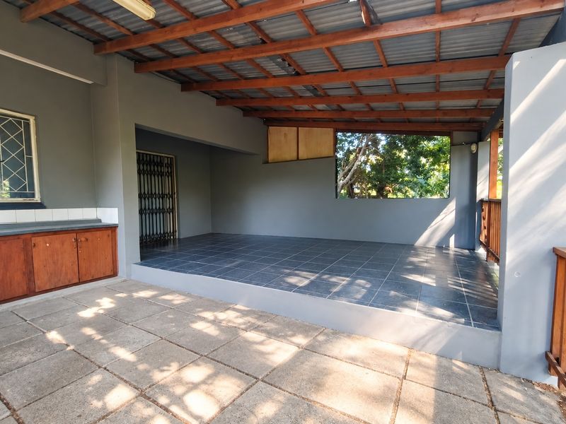 A spacious covered patio featuring tiled flooring, built-in cabinetry, and a timber roof structure, offering a versatile outdoor entertainment area.