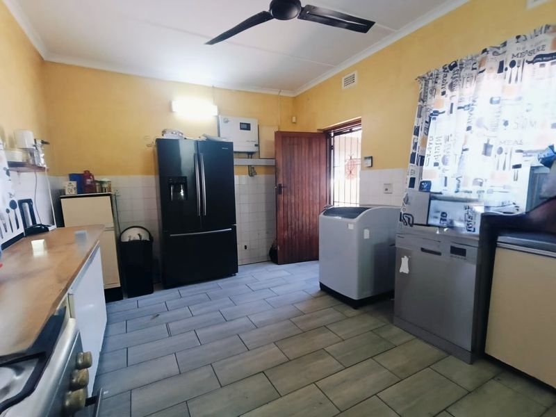 Functional kitchen area featuring tiled flooring, tiled splashbacks, a ceiling fan, and direct access to the exterior via a timber door.