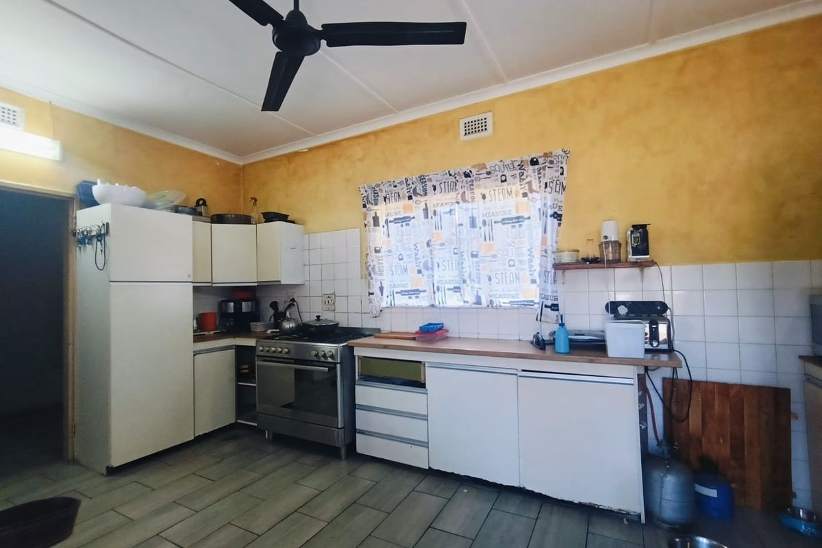 A functional kitchen featuring built-in cabinetry, a freestanding stove, tiled backsplash, and ceiling fan, offering potential for modernization and cosmetic updates.
