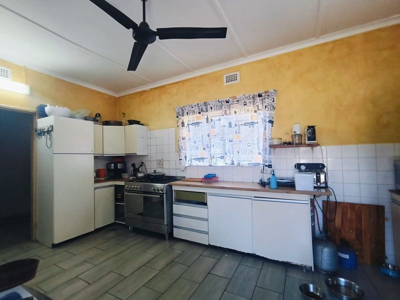 A functional kitchen featuring built-in cabinetry, a freestanding stove, tiled backsplash, and ceiling fan, offering potential for modernization and cosmetic updates.