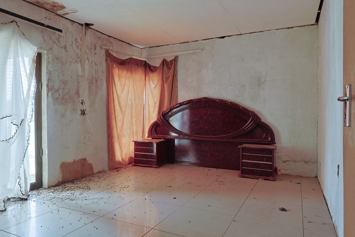 A bedroom in need of significant renovation, featuring tiled floors and a sliding glass door, currently showing extensive wall and ceiling damage.