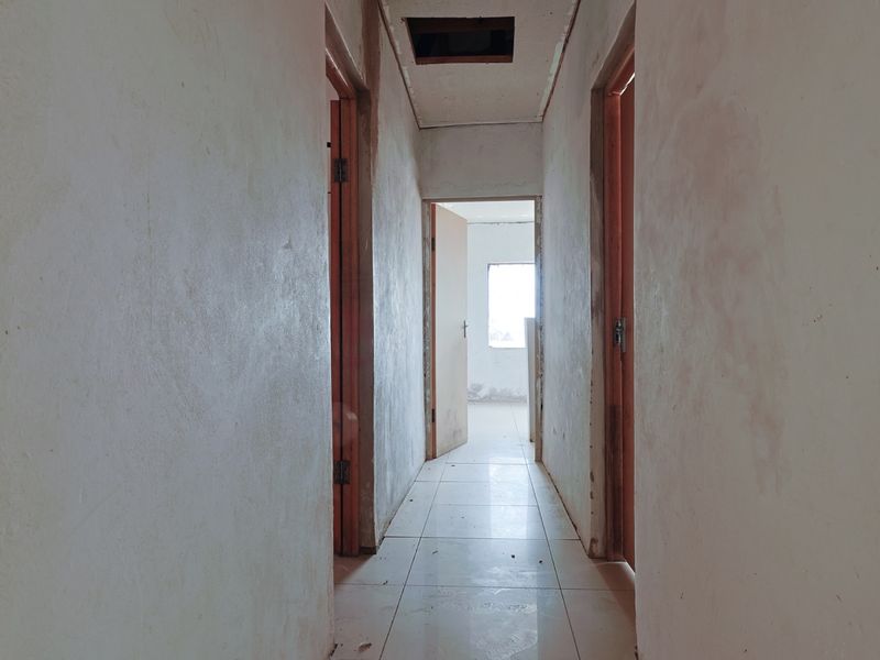 A vacant hallway featuring tiled flooring and wooden door frames, currently in need of cosmetic finishing and maintenance.