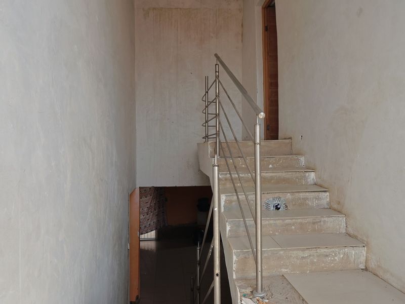 A staircase area featuring a stainless steel balustrade and tiled steps, currently showing signs of wear and requiring cosmetic attention to the surrounding walls.