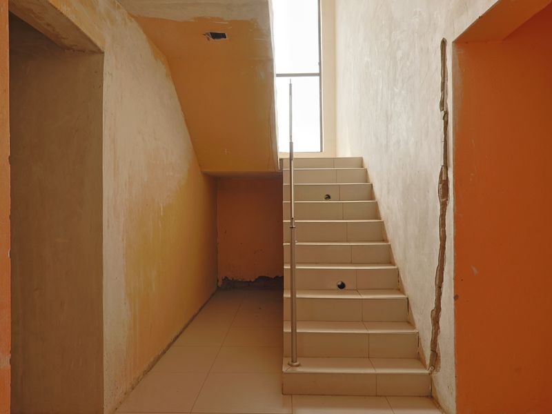 An unfinished interior hallway featuring a tiled staircase with a metal handrail, requiring plastering and finishing work to complete the space.