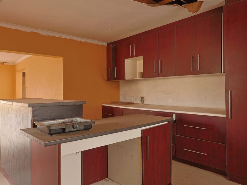 An empty kitchen featuring dark wood-look cabinetry, a central island, and tiled flooring, currently requiring ceiling repairs and general cosmetic updates.