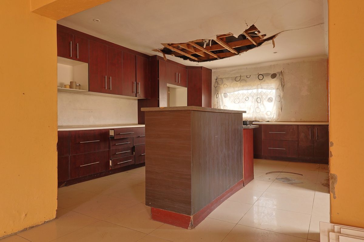 A spacious kitchen featuring dark wood cabinetry and a central island, currently requiring significant ceiling and wall repairs.