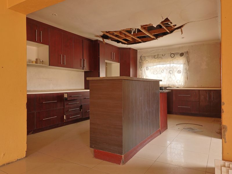 A spacious kitchen featuring dark wood cabinetry and a central island, currently requiring significant ceiling and wall repairs.