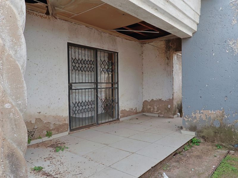 A covered patio area featuring tiled flooring and a security gate, currently showing significant signs of wear and requiring maintenance to the ceiling and walls.